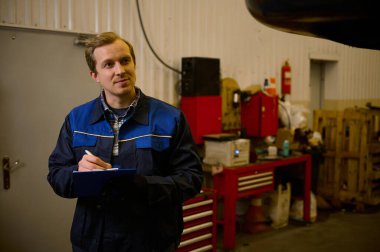 Profesyonel üniformalı genç, beyaz teknisyen mühendis tamir atölyesinde sicil kaydı tutuyor.