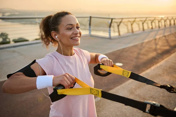 サスペンションストラップ付きピンクのTシャツを着た美しい中年のスポーツ女性は 日の出前の早朝に体重トレーニング屋外を楽しんでいます 健康的な習慣や積極的なライフスタイルの概念 — ストック写真