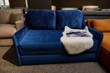 Mobilya mağazasında farklı kalitede ve kumaş dokusuna sahip kanepeler ve kanepeler sergileniyor. Satılık mavi, rahat bir kanepeye odaklan.