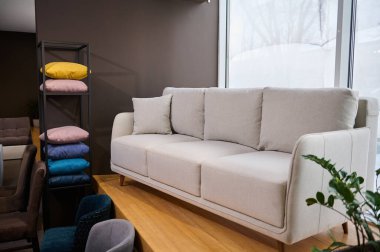 Modern mobilyaların sergilendiği bir galeride sergilenen minimalist beyaz kanepe, farklı dokulardan, yumuşaklıktan, renklerden ve kaliteden gelen renkli yastıklarla ayakta duruyor.