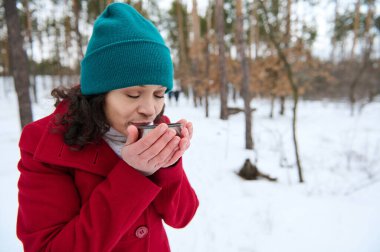 Koyu saçlı, kıvırcık saçlı, beyaz tenli, parlak renkli, ılık kışlık elbiseli, sıcak çay ya da kahve içen, karlı, güzel bir günün tadını çıkaran, karla kaplı bir doğa.