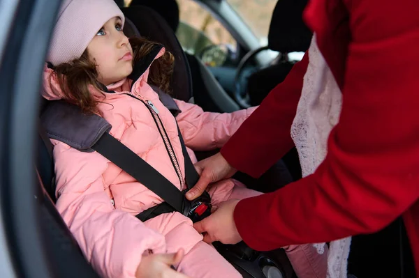 ピンクのパステルダウンジャケットの愛らしい白人の少女は 家族の車の中で子供の助手席に座って ベルトで彼女を締め彼女のお母さんを見ています 車で旅行中の子供の安全保障 — ストック写真