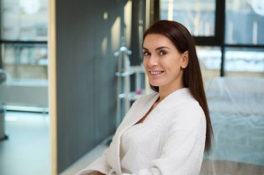 Yüzünde ve vücudunda yaşlanma karşıtı güzellik tedavisi gördüğü için sağlık merkezini ziyaret eden beyaz terry bornozlu çekici orta yaşlı beyaz kadın. Kozmetoloji ve Tıbbi Konsept