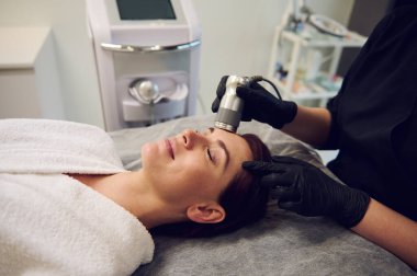 Çekici, orta yaşlı, Avrupalı güzel bir kadının modern sağlık merkezlerinde gençleştirici, cildini temizleyen bir güzellik tedavisi gördüğü yakın plan. Donanım kozmetoloji kavramı