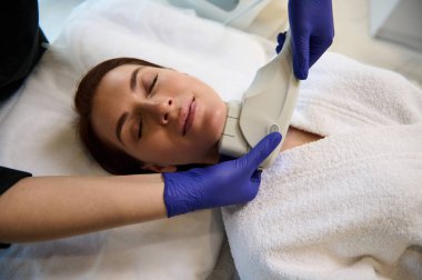 Modern lazer teçhizatı kullanılarak modern sağlık kaplıcalarında yüz bakımı gören beyaz bir kadın. Cihaz kozmetolojisi ve cilt bakımı konsepti. Vücut bakımı, cilt bakımı