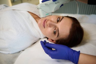 Modern Sağlık Spa Kliniği 'nde cilt bakımı yapan genç ve güzel bir kadın. Modern ekipmanlarla lazer tedavisi. Donanım kozmetolojisi. Ultrasonik temizleme ile yüz temizleme prosedürü