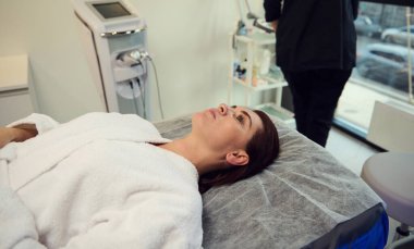 Kozmetik kliniğinde masaj koltuğunda uzanmış güzel beyaz bir kadın. Yaşlanma karşıtı, gençleştirici bir güzellik tedavisine hazır..