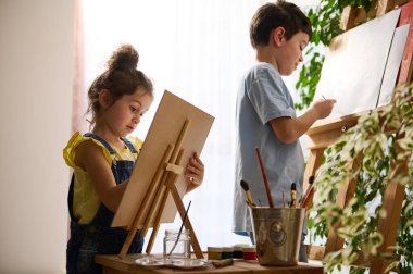 Güzel, zeki çocuklar, sanat dersinden zevk alan anaokulu çocuğu, yağlı boya ve suluboya resimlerle tuvale resimler çiziyor. Yaratıcılık, eğitim, sanat, çocuk eğlencesi, hobi kavramı