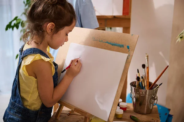 Adorable sweet baby girl, talent Caucasian child drawing picture on canvas. Art class, creativity, motor skills development, creativity and kids education concept