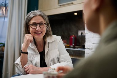 İki nesilden iki farklı insan bir masada oturup sohbet ederken rahat bir moda stüdyosunda kahve içiyor.
