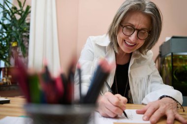 Mutlu gülümseyen Kafkas kadın moda tasarımcısının bulanık renkli kalem tutucusuna bakın. Yaratıcı bir moda stüdyosunda eskiz çizimi yapmak için yeni kıyafet tasarımcıları yaratıyor.