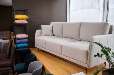 Modern mobilyaların sergilendiği bir galeride, farklı dokulardan, yumuşaklıktan, renklerden ve kaliteden renkli yastıklarla sergilenen şık minimalist beyaz kanepe.