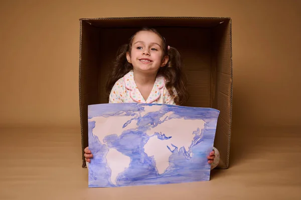 美しい小さな女の子と2つのポニーテールがポストカードボックスの中に座っています ベージュの背景に隔離された世界地図と絵のイメージ 環境保全と地球の概念を保存 — ストック写真