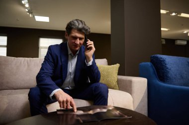 İç mimar, satış temsilcisi, mobilya mağazasında başarılı bir perakende müdürü katalog sayfalarını karıştırıyor ve telefonda müşteriye danışıyor, kanepede oturuyor. Ev geliştirme kavramı