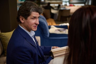 Mobilya mağazasındaki yakışıklı satış temsilcisi bir kanepenin döşemesi için renkli kumaş örneklerini alıcıya sunar. Ev geliştirme, iç tasarım, küçük işletme