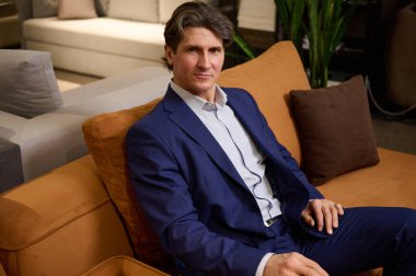 Yakışıklı, olgun Avrupalı bir kadının kendine güvenen portresi, bir mobilya mağazasında otururken koltuğun kalitesini ve sertliğini test eden iş elbiseli bir müşteri. Küçük işletme, ev iç tasarımı