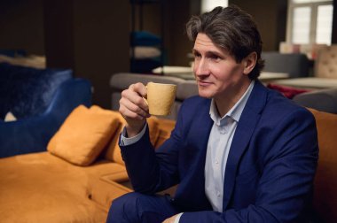 Mobilya mağazası müşterisi, takım elbiseli yakışıklı adam kanepede oturup ev dekorasyonu projesiyle ilgili bir iç mimarın görüşünü bekliyor.