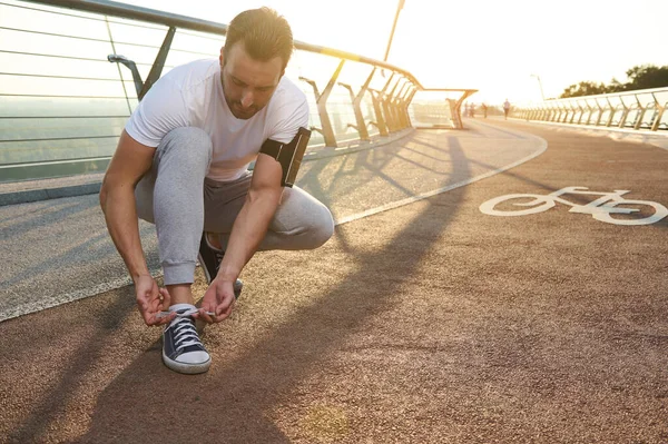 中年の白人男性アスリートジョガー夜明けの朝のジョギング中にトレッドミルで靴ひもを結ぶ 心臓トレーニング ジョギング ランニング 屋外スポーツトレーニング 持久力の健康的なライフスタイルの概念 — ストック写真