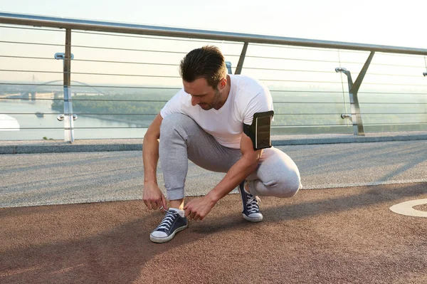 中世の白人スポーツマン選手ランナーが靴ひもを結んで街のガラスの橋の上に立って朝のジョギングの準備ができて — ストック写真