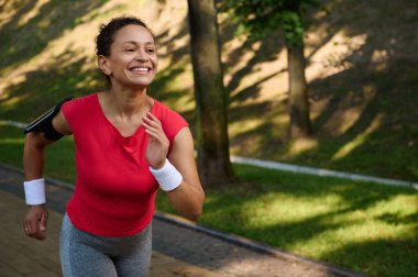 Yakın plan Afro-Amerikan formda bir kadın, sıkı spor giyimli bir atlet bir şehir parkında koşu bandında koşuyor, güneşli bir yaz gününde kardiyo çalışmasının keyfini çıkarıyor.