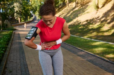 Orta yaşlı, fit bir kadın, koşucu, sporcu kadın karnını tutuyor, yan krampları var, antrenman sırasında ağrısı var. Spor sakatlıkları konsepti