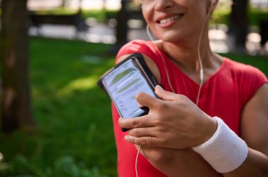 Bulanık gülümseyen bayan sporcunun kolundaki akıllı telefon tutucusuna odaklanın. Sabah koşusu sırasında parmağını telefona koyup mobil uygulama ve çalma listesini ayarlayın. Spor ve aletler