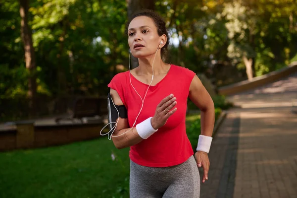 Çekici, bitkin, güçlü kaslı İspanyol sporcu, sporcu, sağlıklı, güzel estetik vücut yapısı olan koşucu şehir parkında koşuyor, güneşli yaz gününde sabah koşusunun keyfini çıkarıyor.