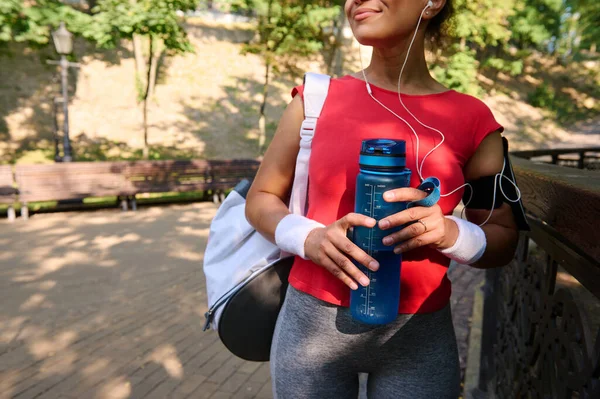 Çekici bir sporcunun ellerine odaklan. Güzel, dişlek bir gülümseme, elinde bir su şişesi, ve şehir parkında idmandan sonra dinleniyor. Spor, aktif yaşam tarzı ve spor konsepti