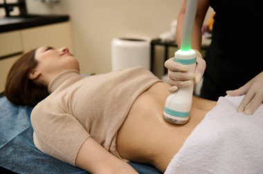 Temas jeli üzerinde hareket eden ultrasonik bir güç çeviriciye odaklanın. Vücut şekillendirme terapisi gören sağlıklı genç bir kadının yağlanmış göbeği. Spa kliniğinde. Profesyonel anti-selülit vücut bakımı