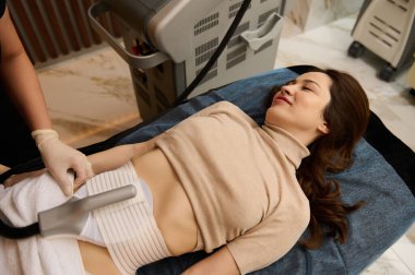 Beautiful woman in medical spa receiving a non surgical body contouring and body sculpting using a modern newest lipo laser equipment. Anti-cellulite treatment, body and skin care concept