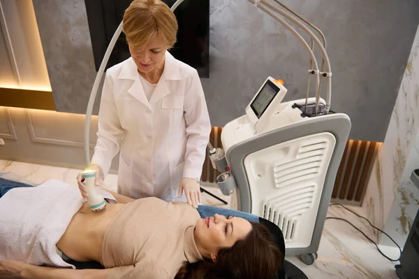 Çekici, estetik vücutlu esmer, estetik olmayan, cerrahi olmayan vücut şekillendirme ve anti-selülit terapisi alan, sağlık kliniğindeki deneyimli beyaz kadın estetisyen kadın.