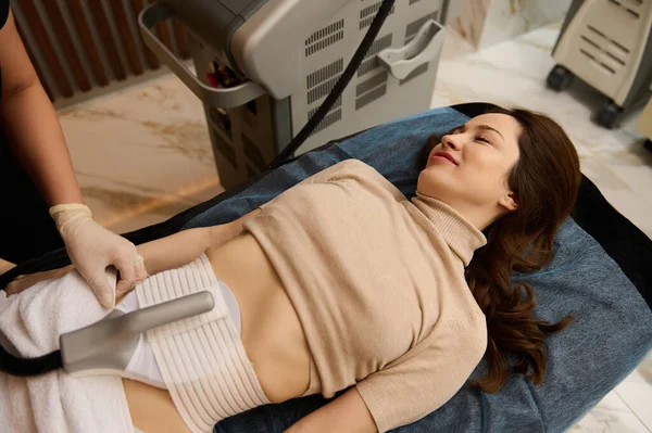 Beautiful woman in medical spa receiving a non surgical body contouring and body sculpting using a modern newest lipo laser equipment. Anti-cellulite treatment, body and skin care concept