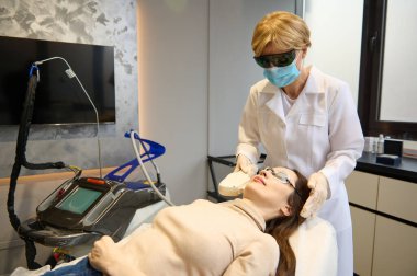 Güzellik uzmanı bir güzellik salonunda lazer gençleştirme yapıyor. Elos epilasyon tüy çıkarma prosedürü bir kadının yüzünde. Güzellik uzmanı bir güzellik salonunda lazer gençleştirme yapıyor. Yüz derisi