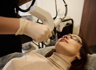 Avrupalı orta yaşlı bir kadının yüz lazeri parlatma ve gençleştirme ameliyatı olurken, kozmetolog donanım aparatı kullanıyor.