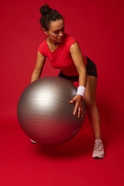 Orta yaşlı Afrikalı Amerikalı sporcu kadın reklam metinleri için reklam alanı olan kırmızı arka planda fitness topuyla egzersiz yapıyor.