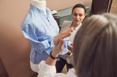 Dikkatimizi, terzilik ve moda atölyesindeki manken mankeni üzerine yeni giysi koleksiyonu üzerinde çalışan orta yaşlı, çekici İspanyol moda tasarımcısı terzisine verelim.