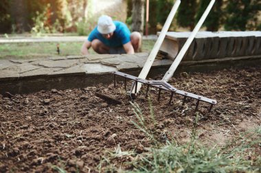 Bahçe küreğine odaklan ve gevşek zeminde tırmıkla ve bulanık arka planda tarlada çalışan çiftçi. Tarım işi. Yeni tarım ekme mevsimi. Tarım endüstrisi. Tarım, organik tarım