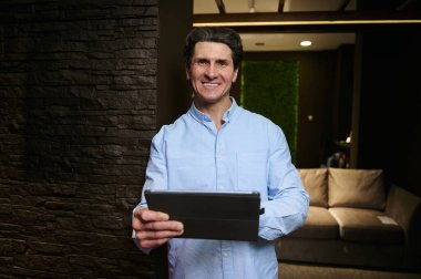 Başarılı Avrupalı orta yaşlı işadamı, girişimci, iç mimar, yeni bir iş projesi planlayan satış müdürü, loş ışıkla aydınlatılmış şık iç mekanlarda dijital tablet üzerinde çalışıyor.