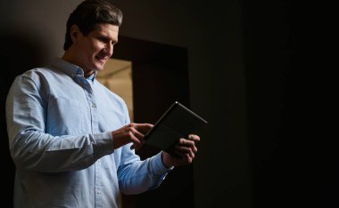 Dijital tablet üzerinde çalışan, mavi günlük gömlekli, yakışıklı, olgun bir beyaz adamın kendine güvenen portresi. Emlakçı, iç mimar, başarılı iş adamı, girişimci, satış müdürü..