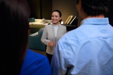 Müşterilerin omuzlarından büyüleyici bir Afrikalı Amerikalı kadın satış temsilcisine, iç mimar, bir mobilya mağazasında danışmanlık yaparken dişlek gülümseyerek gülümseyen bir yöneticiye bakın.