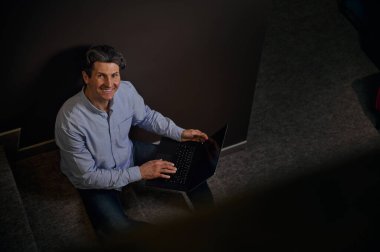 Kendine güvenen, olgun, olgun, beyaz bir iş adamı, girişimci, dizüstü bilgisayarda çalışan bir metin yazarı, bir evin içinde oturuyor ve kameraya gülümseyen dişlek bir gülümseme.