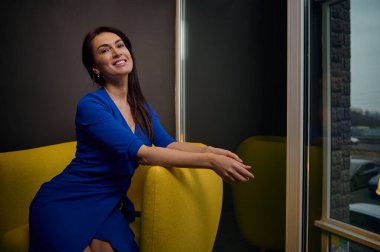 Çekici, koyu renk saçlı Avrupalı bir kadının portresi. İç mimar, iş kadını, emlakçı, satış temsilcisi, modern ofisinde gülümseyen dişlek bir müdür.