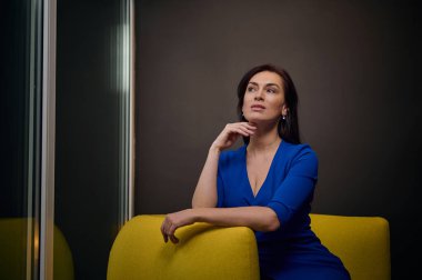 Başarılı bir kadın mavi günlük elbiseler içinde yaratıcı bir ofisin, iç mimari stüdyosunun ya da emlak acentesinin geniş penceresinden dışarı bakıyor.