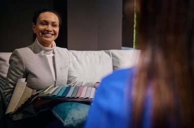 Çekici Afrikalı Amerikalı kadın, başarılı satış müdürü, müşterilerle çalışan iç mimar, çeşitli dokulardan ve koltuk döşemesi kalitesinden çeşitli örnekler gösteriyor.