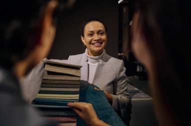 Güler yüzlü Afro-Amerikan iç mimar, mobilya tasarım salonunda satış görevlisi müşterilere kumaş örnekleri, doku ve kalite örnekleri gösteriyor. Ev dekorasyonu kavramı