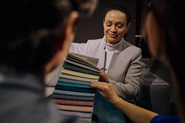 Confident clerk, saleswoman in interior design showroom showing to customers fabric samples for sofa restoration and upholstery of various colors, textures and quality. Home improvement and renovation