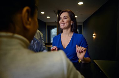 Orta yaşlı, sıradan mavi elbiseli esmer bir kadının ev projesini bir iç tasarımcıyla tartışması ve mobilya mağazasında yeni mobilyalar sipariş etmesi.