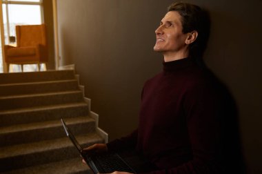 Koyu kahverengi duvar arka planına karşı dizüstü bilgisayarla çalışan yakışıklı beyaz bir adamın yan portresi. İş adamı, girişimci, metin yazarı, gazeteci, serbest yazar. Çevrimiçi iş kavramı. Uzayı kopyala