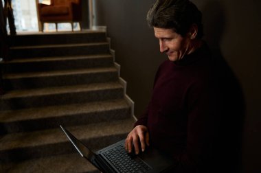 Yaratıcı bir modern iş merkezi koridorunda merdivenlerde dururken dizüstü bilgisayar kullanan başarılı bir adamın, iç tasarımcının, iş adamının, serbest çalışanın portresi.