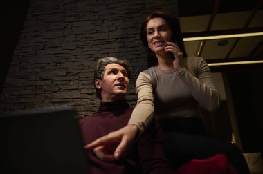 Güzel çoklu görev yapan kadın cep telefonuyla erkek arkadaşının ya da iş ortağının yanında oturmuş rahat, modern bir yaratıcı ofiste dizüstü bilgisayar ya da iş projesi üzerinde çalışıyor.